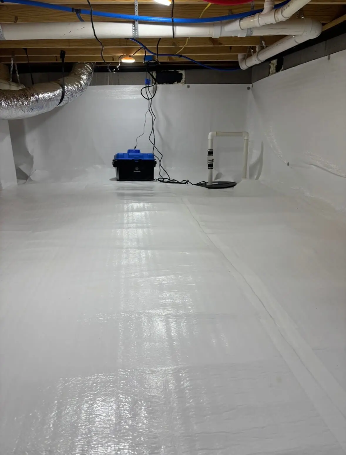 A close-up view of a gray industrial dehumidifier sitting on black risers in a clean, encapsulated crawl space, with insulated ductwork and fiberglass insulation visible overhead.