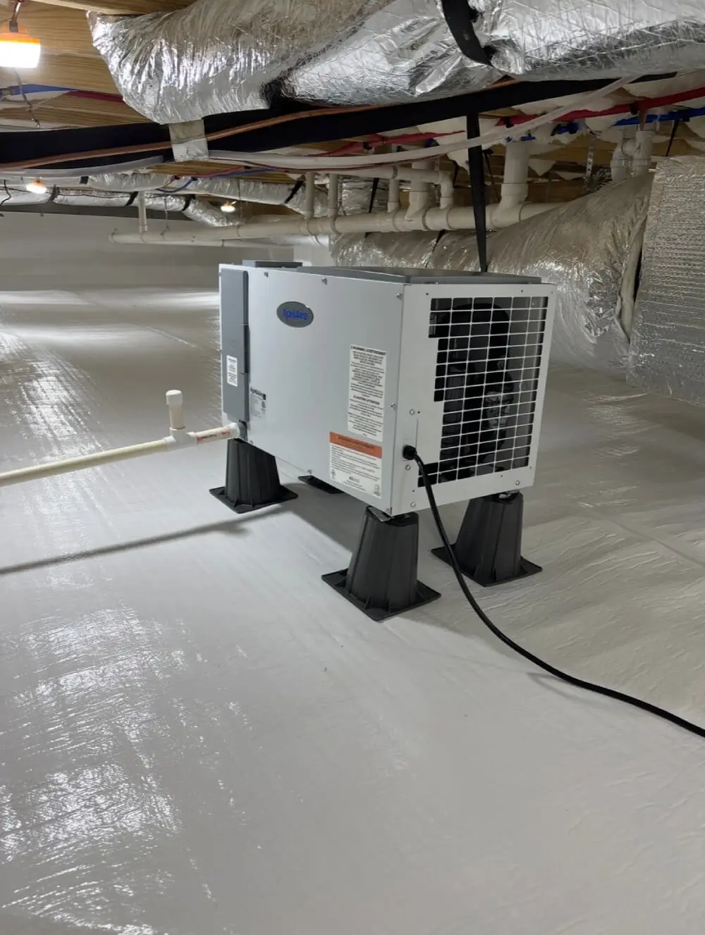 A long perspective of a clean encapsulated crawl space showcasing the continuous white vapor barrier on the floor and the contrast with the thick fiberglass insulation and wooden joists overhead.