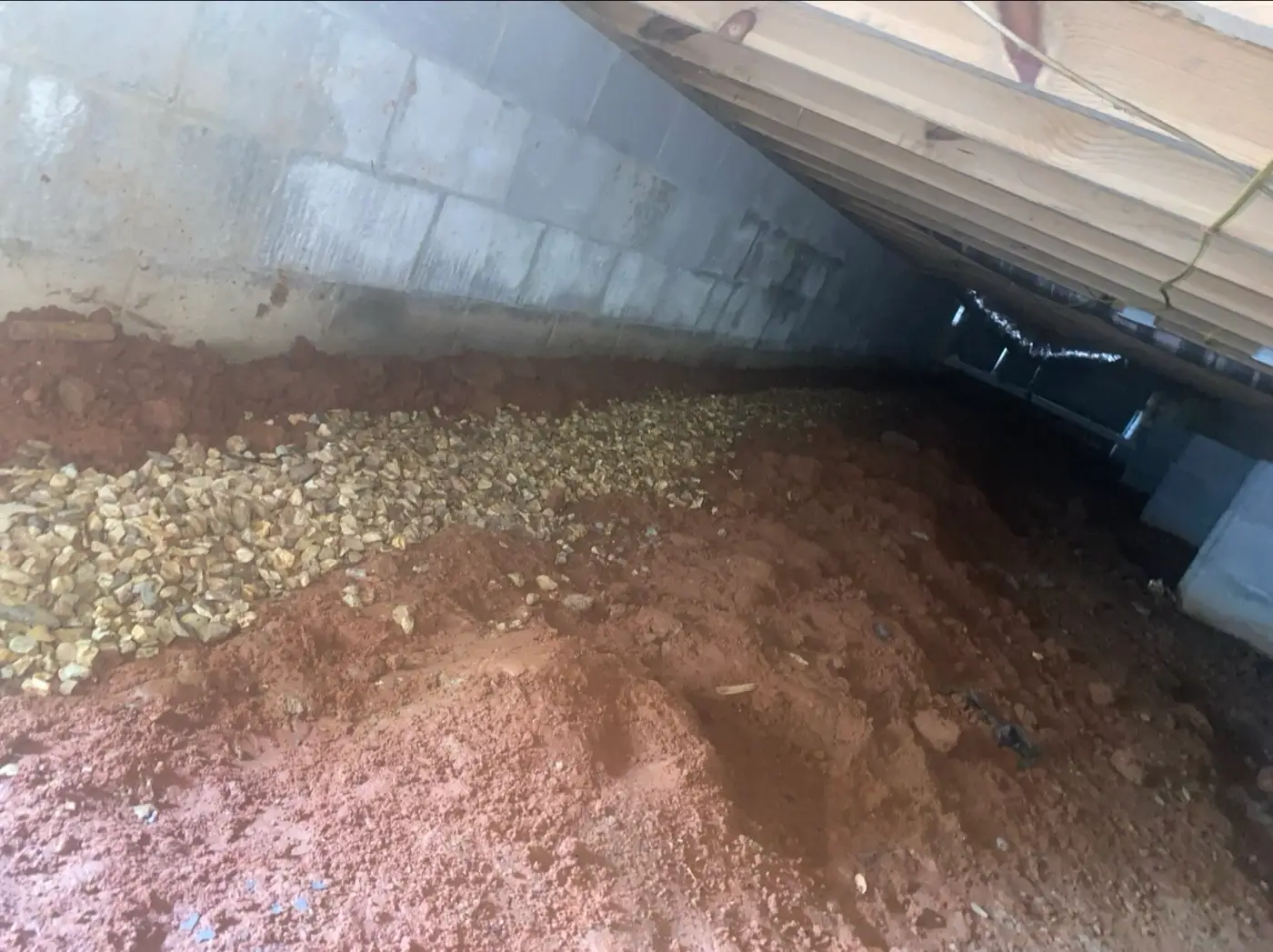 Interior perimeter drainage trench filled with gravel along a concrete block foundation wall in a red clay crawl space
