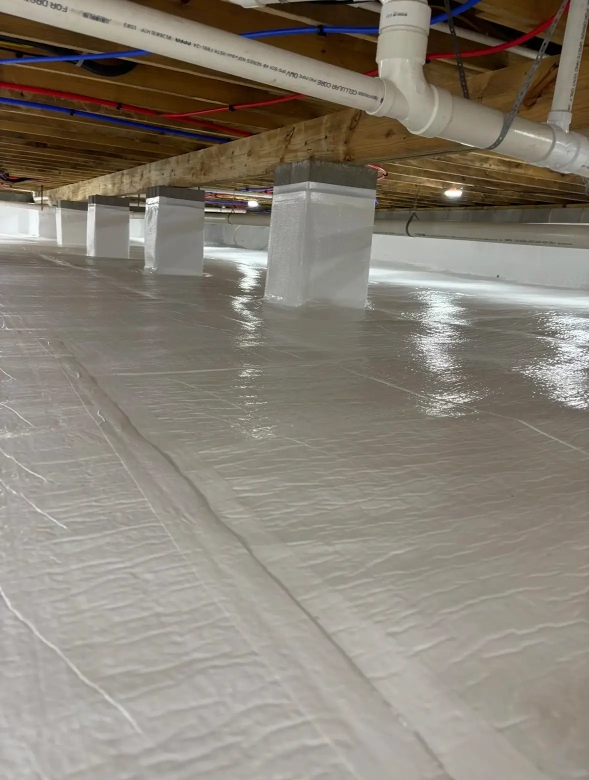 Vapor barrier wrapped around block support piers in a sealed crawl space under PVC plumbing lines