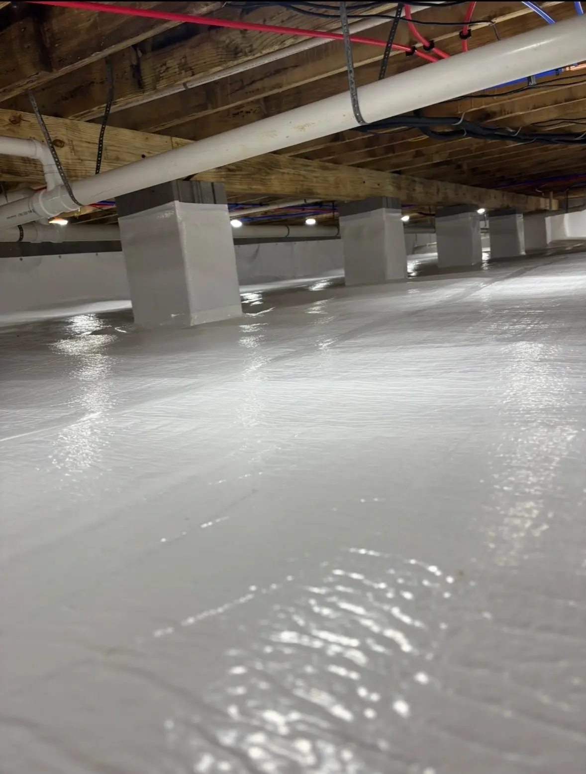 Encapsulated crawl space with vapor barrier sealed to the support piers and plumbing running overhead