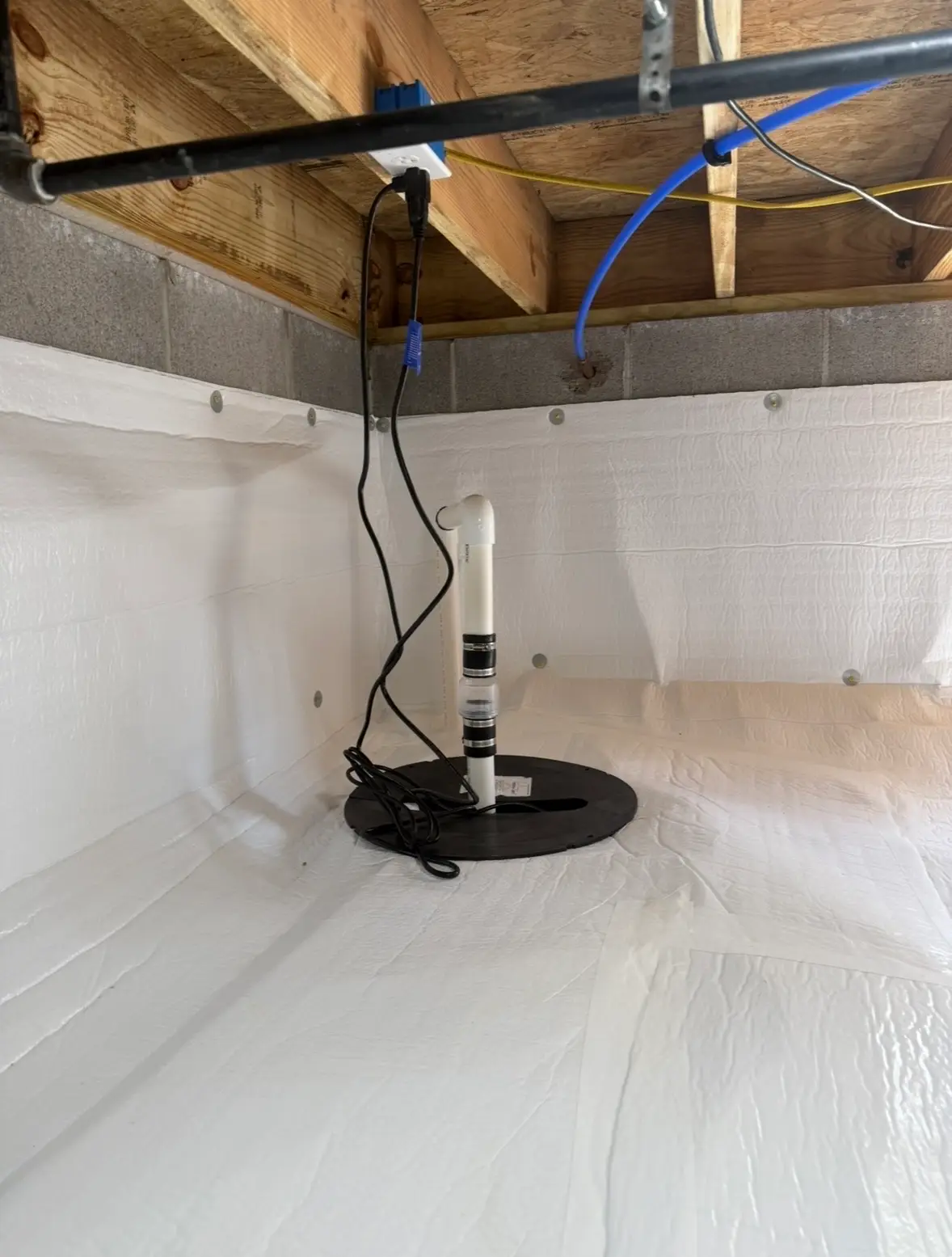 Sealed sump pump basin with PVC discharge pipe in a crawl space lined with white vapor barrier