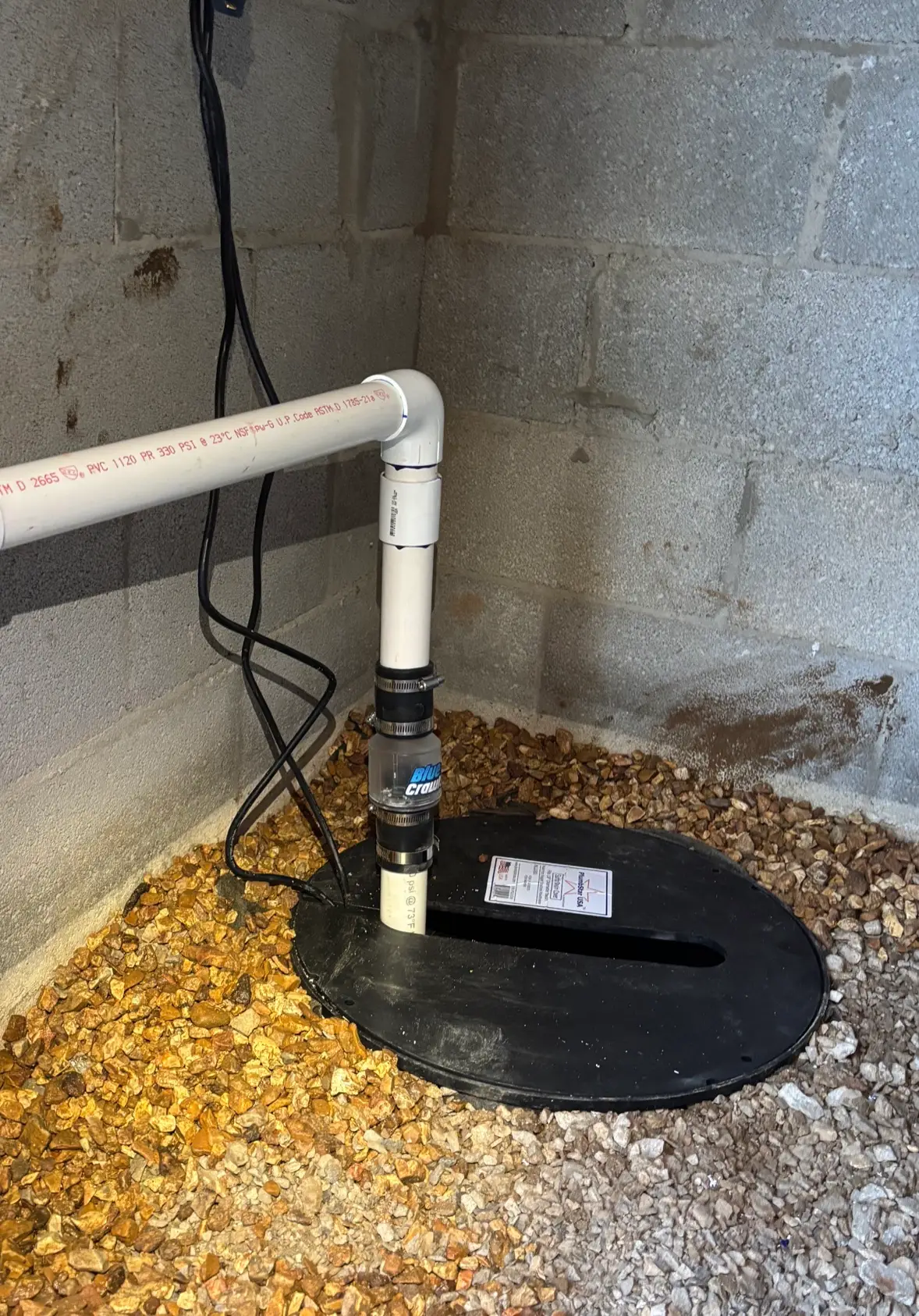 Crawl space sump pump basin set in gravel with check valve and PVC discharge line, before the vapor barrier is installed
