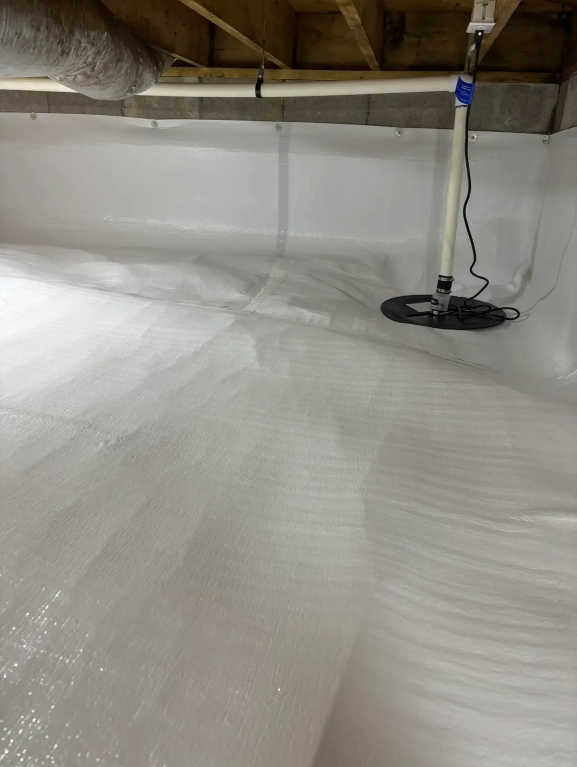 Sump pump with PVC discharge line running up to the joists in an encapsulated crawl space